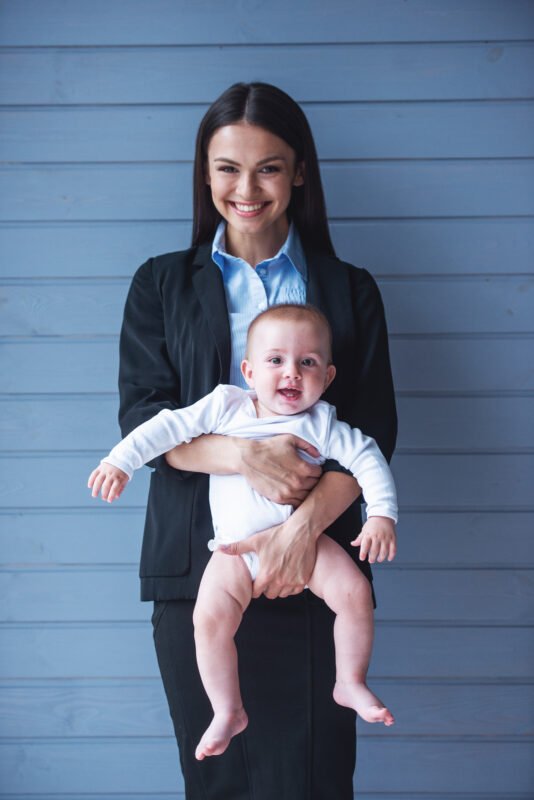 Nounou tenant un bébé devant une maison – garde d’enfants Luxembourg